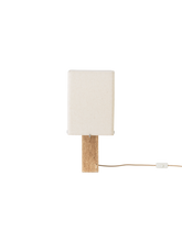 Load image into Gallery viewer, Front view of the switched-off Nonna Table Lamp, showing its rectangular travertine base and sand-coloured linen shade.
